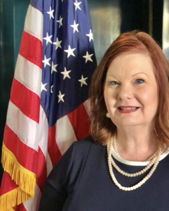 A woman smiling at the camera, standing near the American flag.